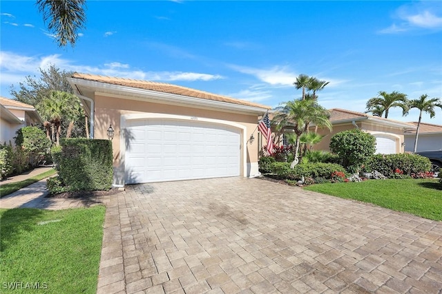 view of front of home with a tiled roof, a front yard, stucco siding, decorative driveway, and an attached garage