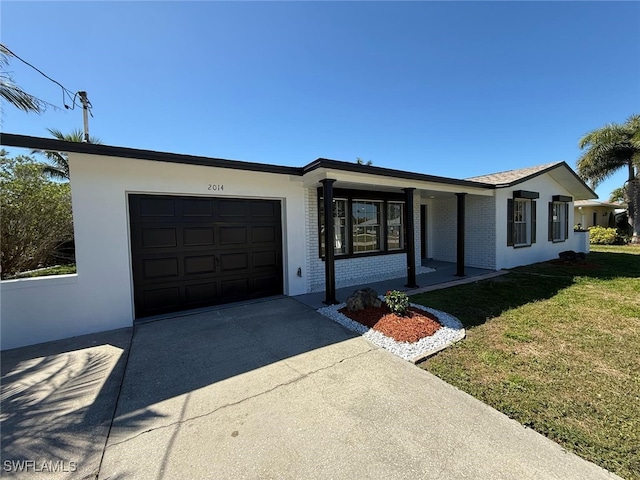 ranch-style house featuring brick siding, an attached garage, a front yard, stucco siding, and driveway