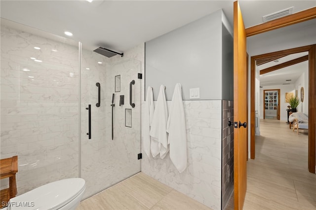 full bath with a marble finish shower, visible vents, toilet, and tile walls