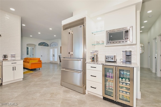 kitchen with light stone countertops, beverage cooler, built in appliances, decorative backsplash, and white cabinets