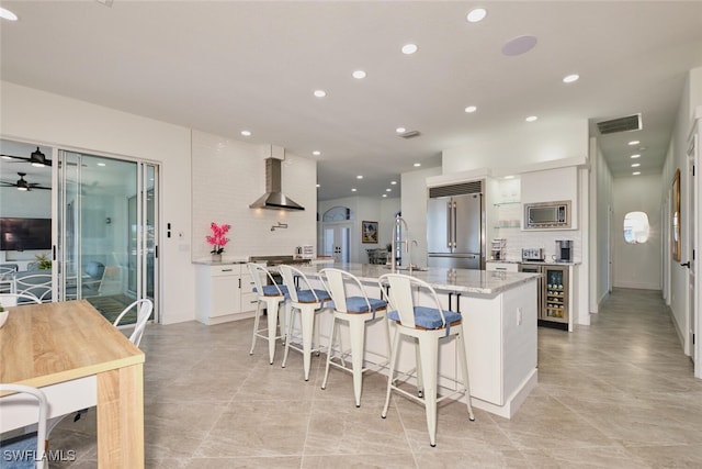 kitchen featuring visible vents, a center island with sink, backsplash, wall chimney range hood, and built in appliances