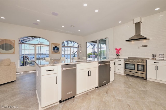 kitchen with a sink, open floor plan, stainless steel appliances, white cabinets, and wall chimney range hood