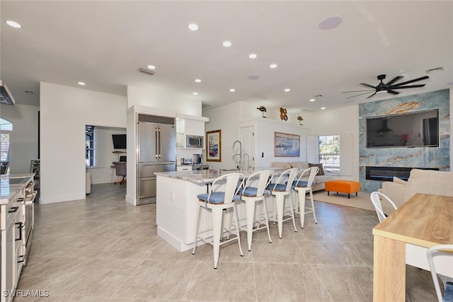 kitchen featuring a ceiling fan, visible vents, a breakfast bar, a kitchen island with sink, and built in appliances