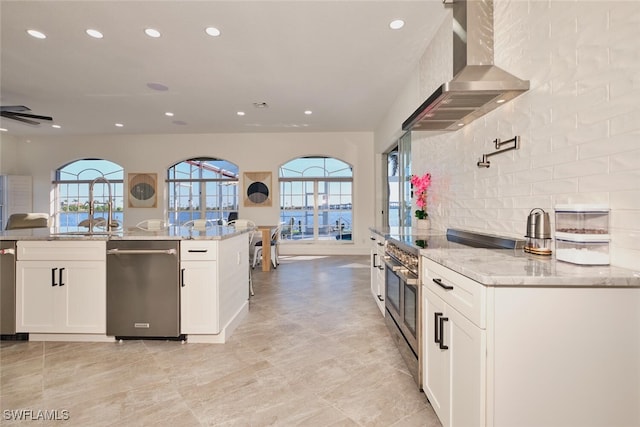 kitchen featuring light stone counters, decorative backsplash, appliances with stainless steel finishes, wall chimney exhaust hood, and a sink