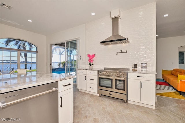 kitchen with visible vents, appliances with stainless steel finishes, white cabinets, wall chimney range hood, and light stone countertops