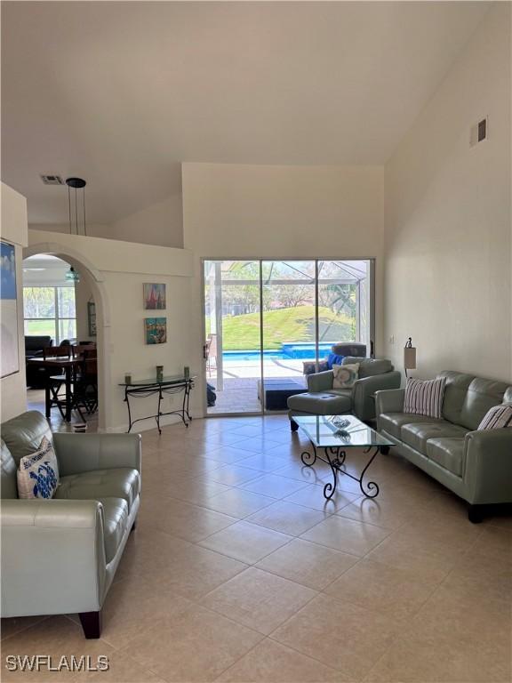 living room featuring light tile patterned floors, arched walkways, visible vents, and high vaulted ceiling