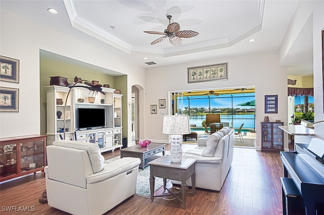 living room with a raised ceiling, arched walkways, dark wood-style floors, and crown molding