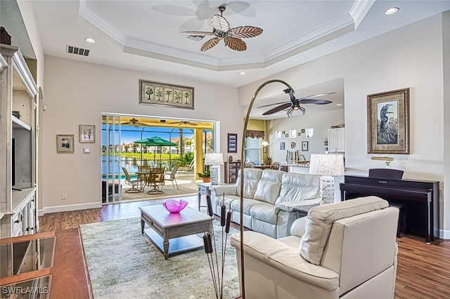 living room with a tray ceiling, visible vents, ceiling fan, and ornamental molding