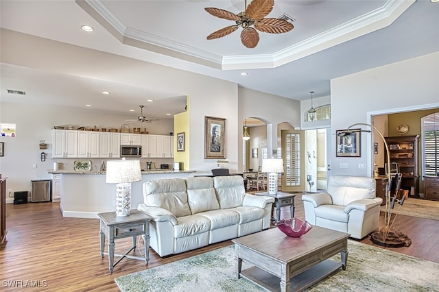 living area featuring crown molding, ceiling fan, a tray ceiling, wood finished floors, and arched walkways