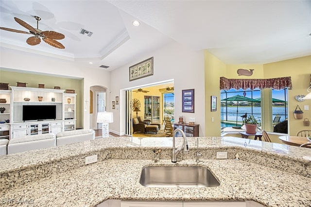 kitchen with arched walkways, light stone countertops, open floor plan, and a sink