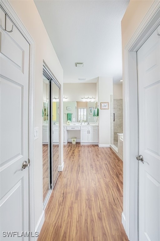 corridor featuring light wood finished floors, visible vents, and baseboards