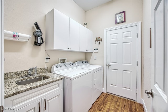 clothes washing area with a sink, cabinet space, wood finished floors, and washer and dryer