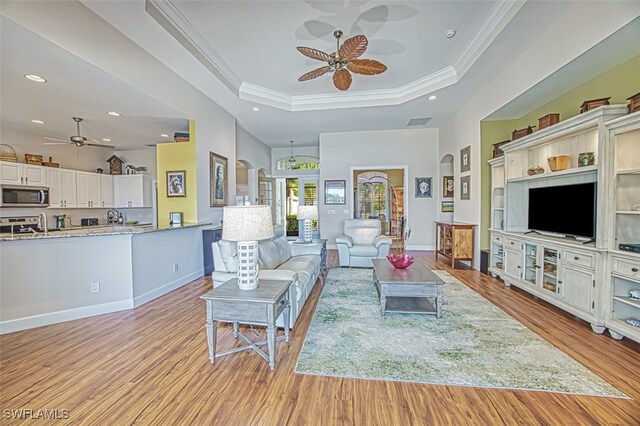 living room featuring light wood-style flooring, recessed lighting, ceiling fan, crown molding, and a raised ceiling