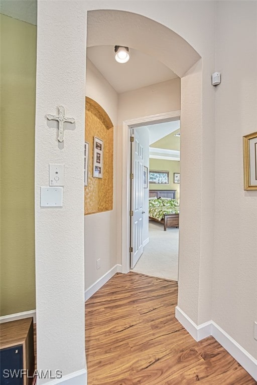 hall featuring baseboards, arched walkways, and wood finished floors