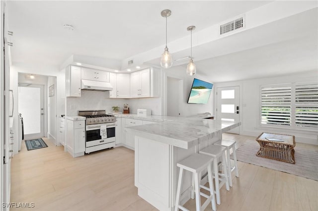 kitchen featuring visible vents, light stone countertops, under cabinet range hood, stainless steel range with gas stovetop, and a peninsula