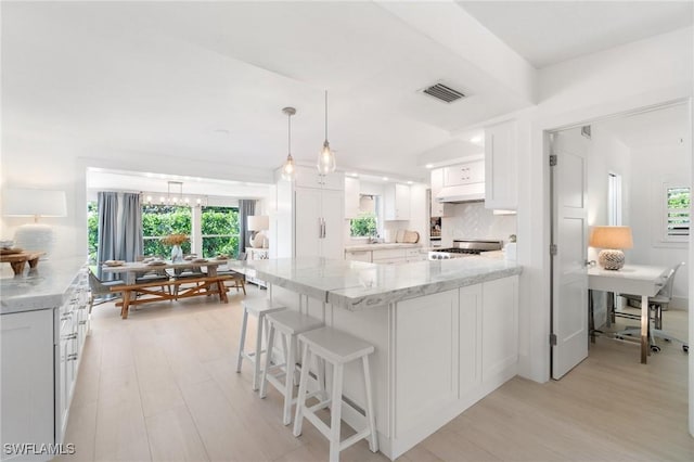 kitchen featuring light stone counters, visible vents, decorative backsplash, stove, and white cabinets