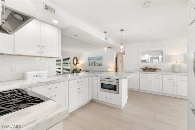 kitchen featuring tasteful backsplash, visible vents, ventilation hood, a peninsula, and white cabinetry