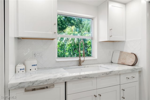 kitchen featuring a sink, light stone counters, tasteful backsplash, and white cabinetry