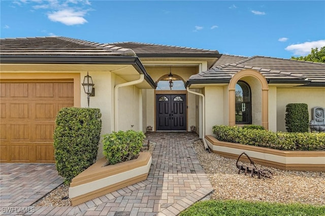 view of exterior entry with stucco siding, an attached garage, and a tile roof