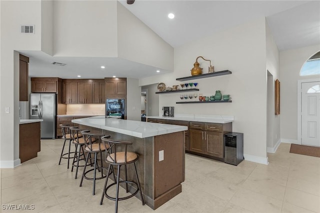 kitchen with visible vents, stainless steel refrigerator with ice dispenser, a breakfast bar area, light countertops, and baseboards