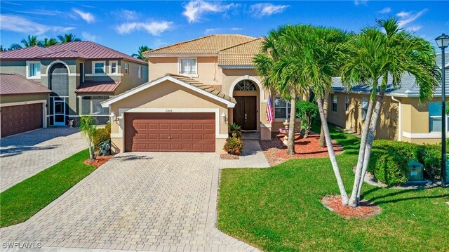 view of front of home featuring a tile roof, a front yard, stucco siding, an attached garage, and decorative driveway