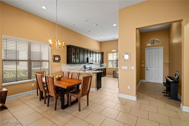 dining space with a towering ceiling, light tile patterned floors, baseboards, and a notable chandelier