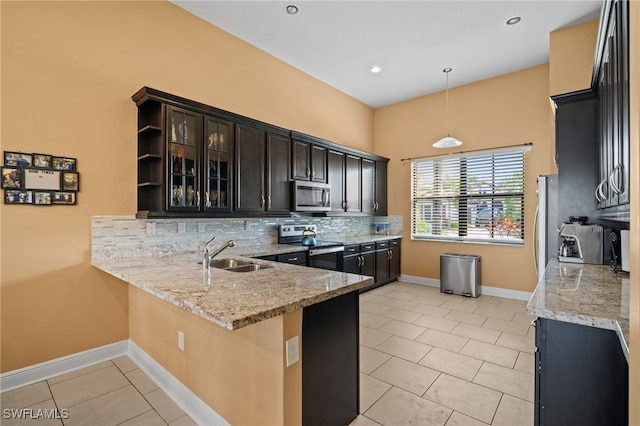 kitchen featuring light tile patterned floors, stainless steel appliances, backsplash, a sink, and a peninsula