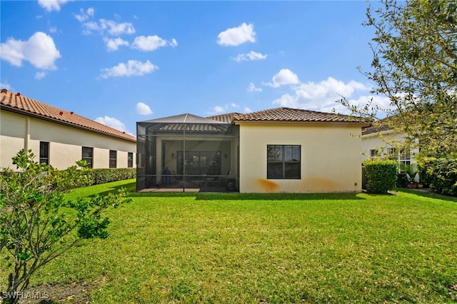 rear view of property with glass enclosure, a lawn, a tile roof, and stucco siding