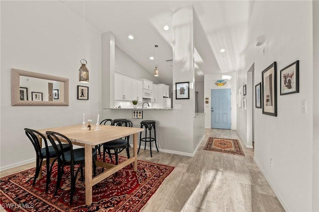 dining area featuring recessed lighting, baseboards, high vaulted ceiling, and light wood finished floors