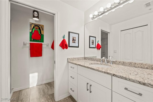 bathroom with visible vents, vanity, baseboards, and wood finished floors