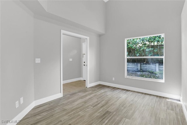 unfurnished room featuring baseboards, wood finished floors, and a towering ceiling