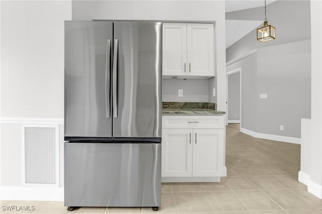 kitchen featuring light stone counters, white cabinets, freestanding refrigerator, and light tile patterned flooring