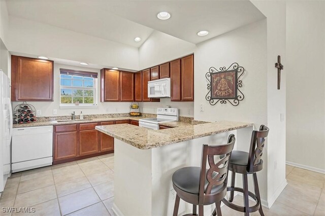 kitchen featuring white appliances, light tile patterned floors, a peninsula, a sink, and a kitchen breakfast bar