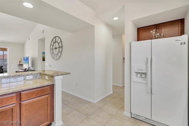 kitchen with light tile patterned floors, light stone counters, brown cabinetry, recessed lighting, and white fridge with ice dispenser