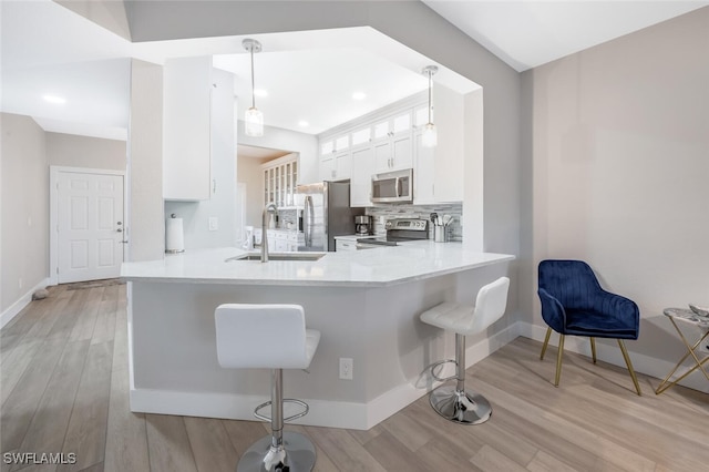 886 Tanbark Dr SW Unit 103, Naples, FL 34108 - kitchen with a sink, appliances with stainless steel finishes, a breakfast bar area, white cabinets, and light wood-type flooring