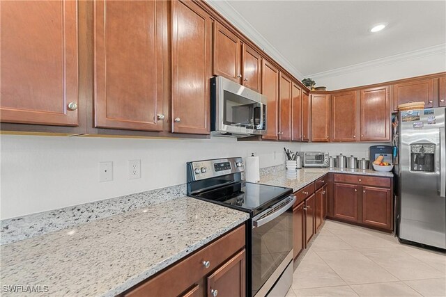 kitchen with light tile patterned floors, light stone countertops, appliances with stainless steel finishes, brown cabinets, and crown molding