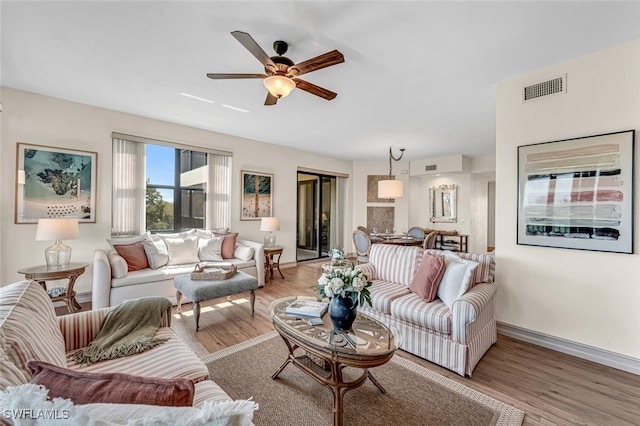 living room featuring visible vents, baseboards, light wood-style flooring, and a ceiling fan