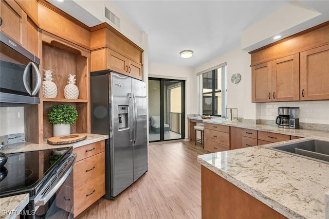 kitchen featuring light stone countertops, open shelves, light wood-style flooring, stainless steel appliances, and decorative backsplash