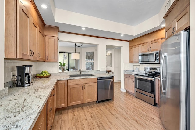 kitchen featuring a tray ceiling, light wood-style flooring, appliances with stainless steel finishes, and a sink