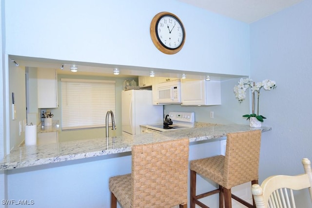 kitchen featuring white appliances, light stone counters, a breakfast bar, a peninsula, and a sink