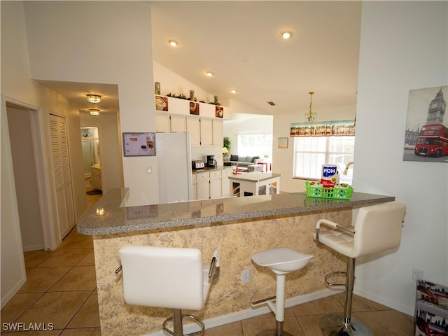 1822 SE 20th St, Cape Coral, FL 33990 - kitchen with freestanding refrigerator, light tile patterned flooring, white cabinetry, a peninsula, and vaulted ceiling