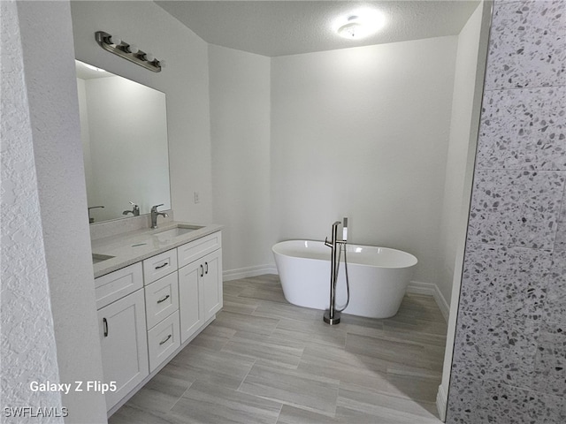 full bath with a sink, a textured ceiling, double vanity, baseboards, and a soaking tub