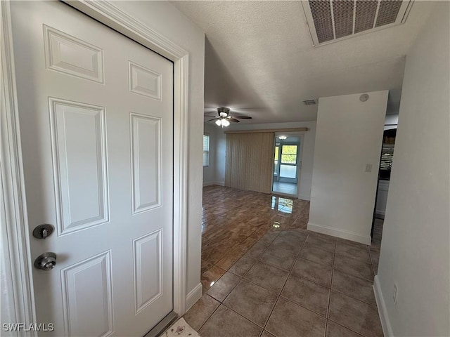 hallway with tile patterned flooring, visible vents, a textured ceiling, and baseboards