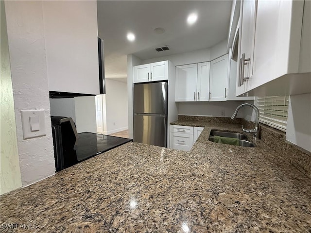 kitchen featuring a sink, dark stone countertops, freestanding refrigerator, white cabinets, and range