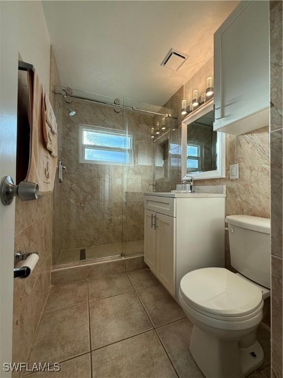 bathroom with a shower stall, toilet, vanity, tile patterned floors, and tile walls