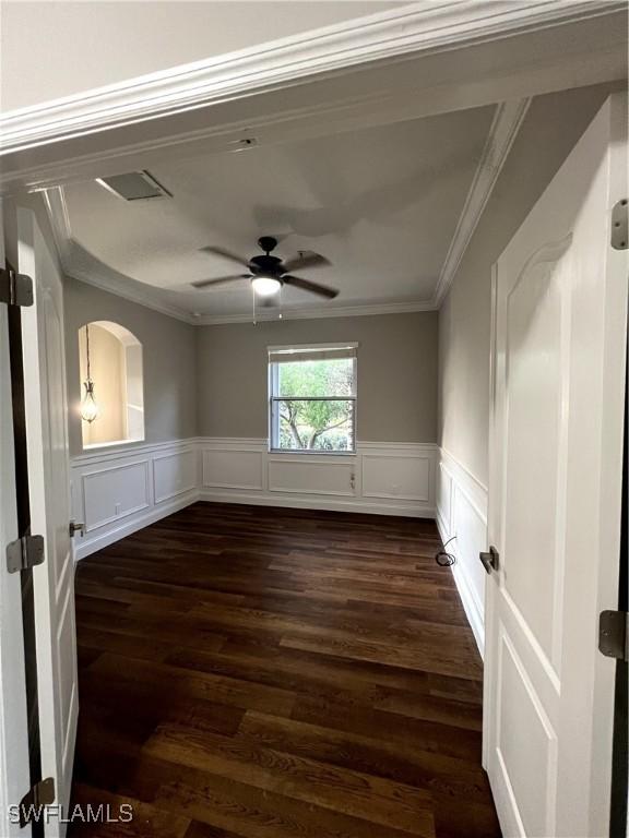 empty room featuring ceiling fan, wainscoting, dark wood-style floors, and crown molding