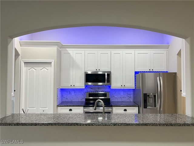 kitchen with tasteful backsplash, white cabinets, stainless steel appliances, and dark stone counters