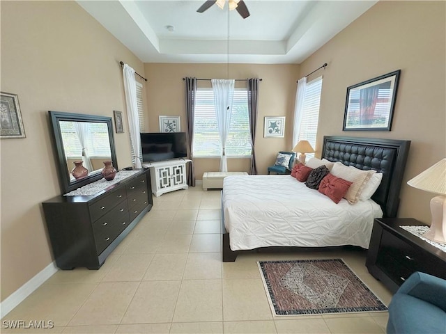 bedroom featuring a raised ceiling, light tile patterned flooring, baseboards, and ceiling fan