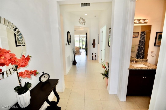 hallway featuring light tile patterned floors, visible vents, baseboards, and a sink