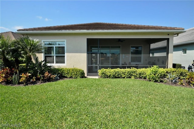 rear view of property with stucco siding, ceiling fan, a yard, and a sunroom